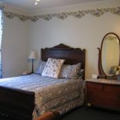 Guest room guest room; white walls with floral banner around ceiling, small wooden bedframe, floral bedspread, wooden dresser with mirror